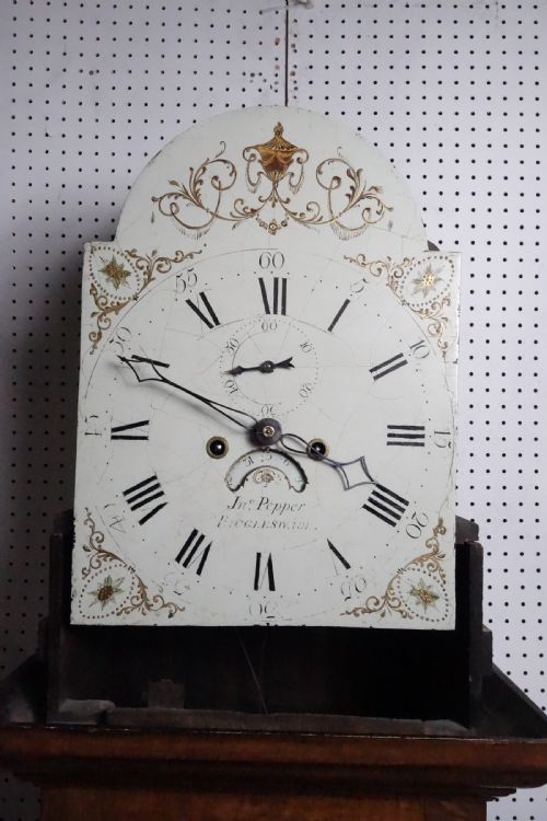 fig 2. Georgian light oak longcase clock hood with brass finials, arched glass door, and white painted dial featuring Roman numerals.