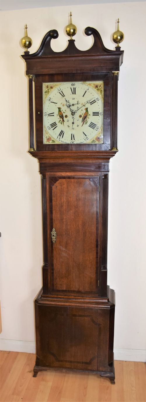 fig 1. A Georgian oak and mahogany crossbanded longcase clock featuring a swan-neck pediment, brass finials, reeded columns, and a hand-painted dial with bird decoration.