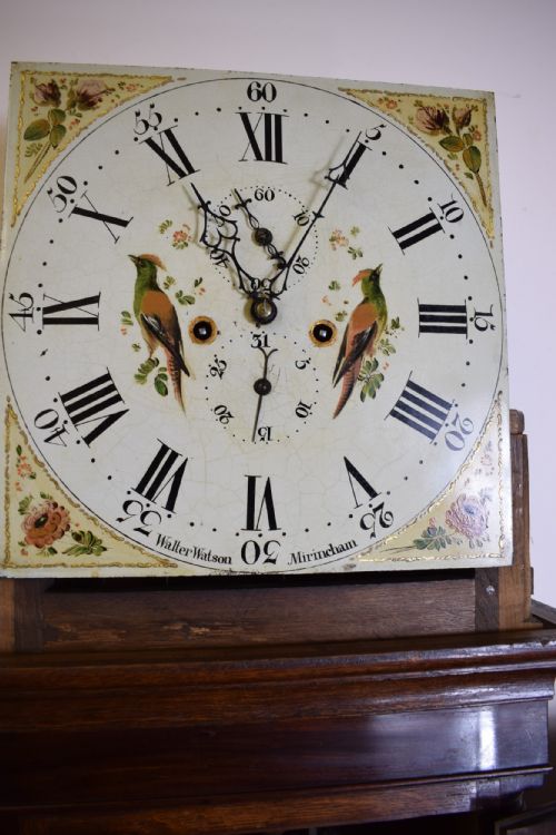 fig 2. A Georgian oak and mahogany crossbanded longcase clock featuring a swan-neck pediment, brass finials, reeded columns, and a hand-painted dial with bird decoration.