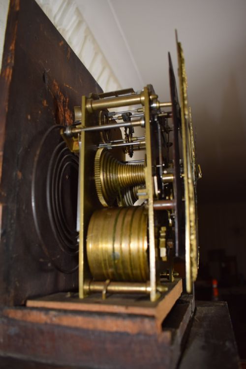fig 2. A dark brown timber grandmother clock featuring a square brass dial framed by glass and flanked by turned columns.