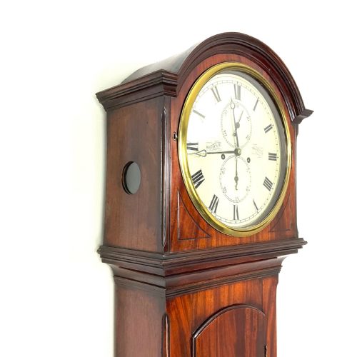 fig 1. A Regency period flame mahogany longcase clock featuring a circular brass bezel, Roman numerals, subsidiary seconds display, and an arched bonnet.