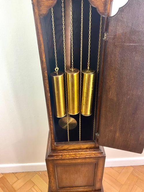 fig 2. A dark oak grandmother longcase clock featuring an arched hood, clear glass door, and a brass dial with Roman numerals.