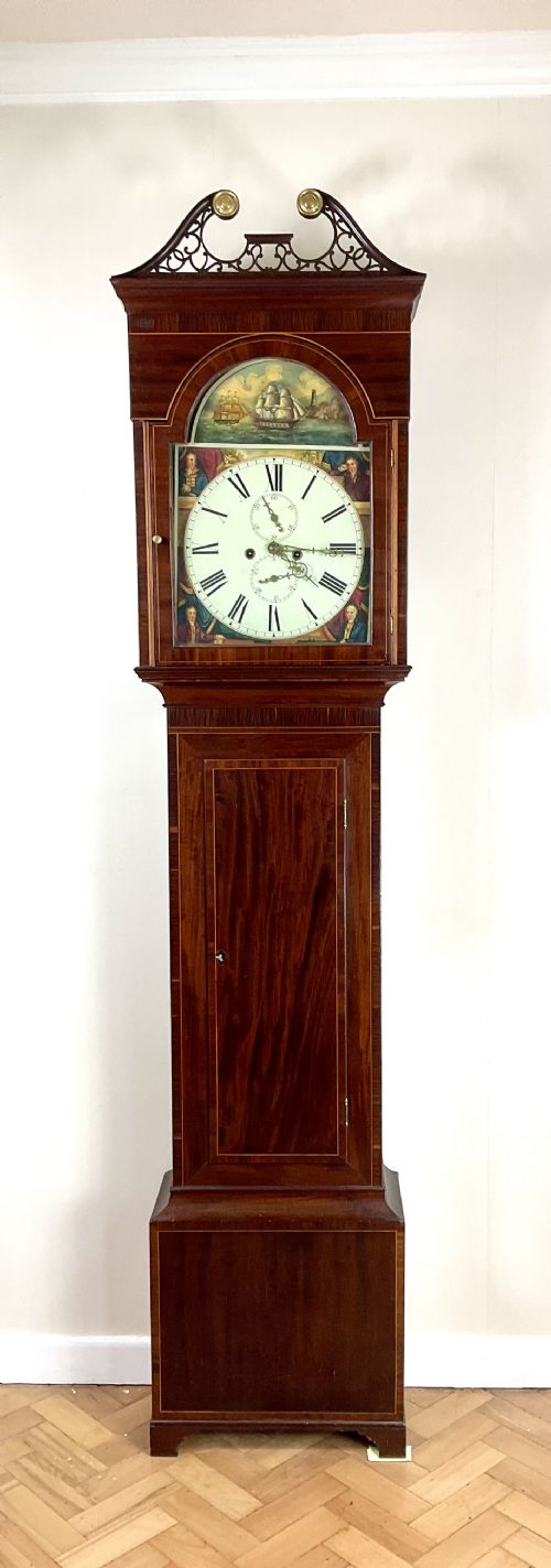 fig 1. An upper hood section of a Georgian mahogany longcase clock featuring open fretwork pediments, brass finials, and a painted arch dial displaying a rocking ship automaton.