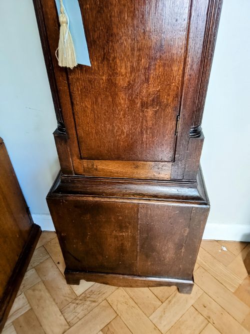 fig 1. An antique Georgian dark oak grandfather clock featuring a swan-neck pediment, fluted columns, an arched trunk door, and a hand-painted floral dial.