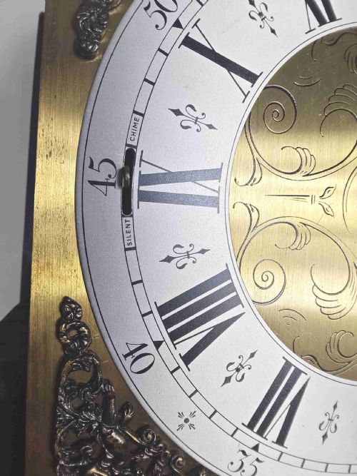fig 2. An English oak longcase clock featuring an arched hood, silvered brass dial, and a glazed trunk door displaying three brass weights and a pendulum.