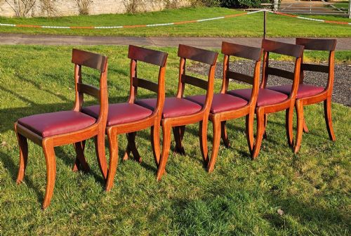 fig 1. A matching set of six Regency mahogany dining chairs featuring curved sabre legs, horizontal bar backs, and burgundy leather seats.
