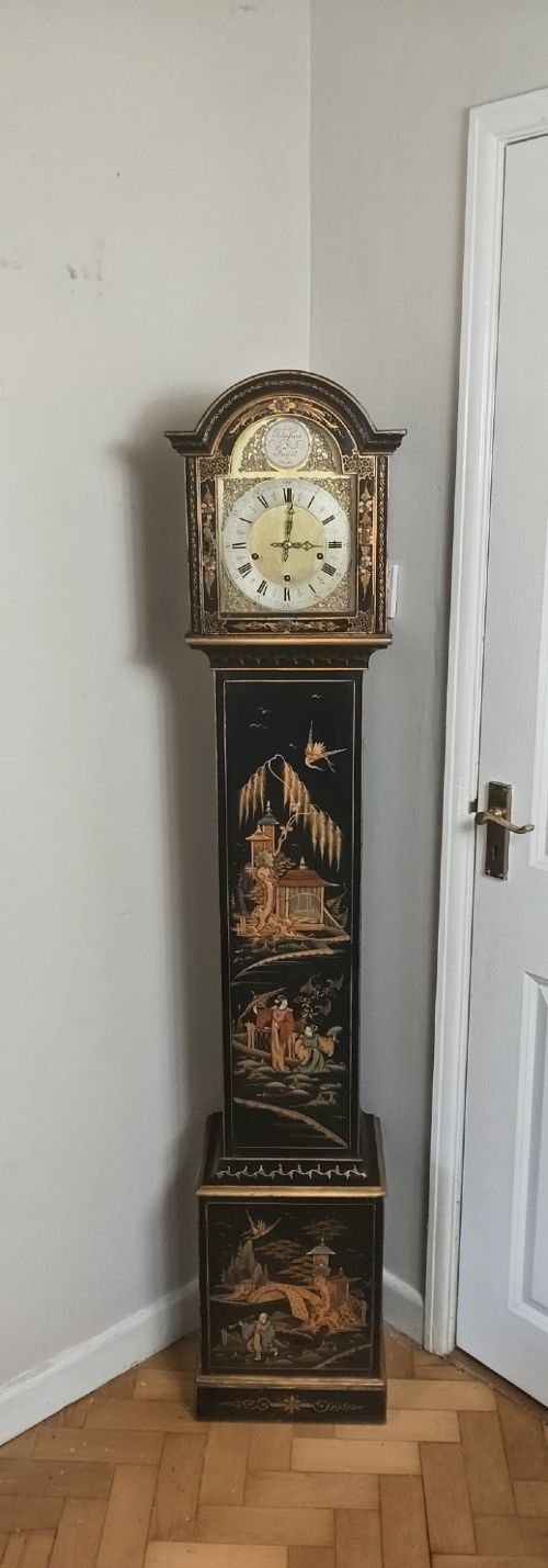 A slender black lacquer grandmother clock decorated with gilded chinoiserie landscape motifs and fitted with an arched brass dial. View VIII