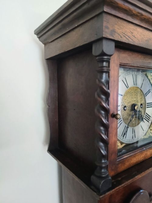 fig 2. A 19th-century dark oak grandmother clock featuring barley twist side pillars, a square glass hood, and a brass dial with Roman numerals.