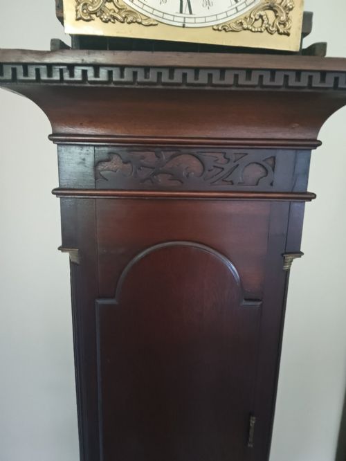 fig 2. A slim dark mahogany longcase clock featuring a swan-neck pediment, brass dial with Roman numerals, and an arched trunk door.