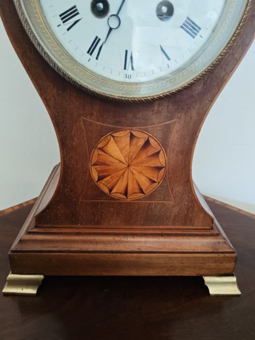 fig 1. An antique balloon-shaped mahogany mantel clock featuring a white enamel dial with Roman numerals, wood marquetry inlay, and small brass feet.