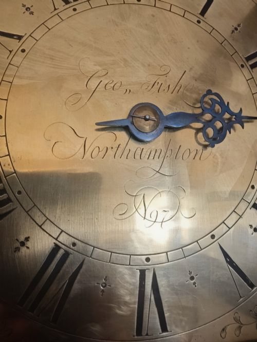 fig 1. A freestanding Georgian oak longcase clock featuring a square brass dial, slender trunk door, turned hood columns, and a square plinth base.