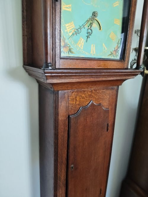 fig 1. A Georgian oak longcase clock featuring a swan-neck pediment, arched trunk door, and a painted duck egg blue square dial with Roman numerals.