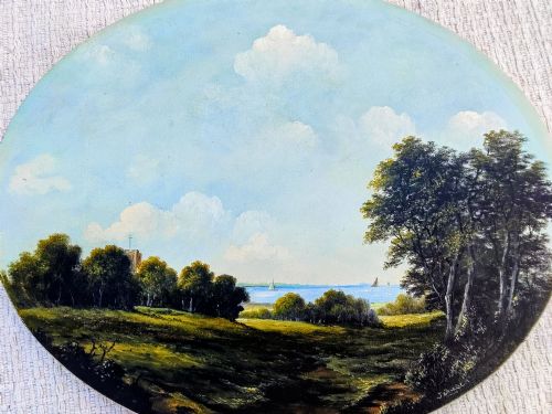 fig 1. An oval oil painting depicting a grassy coastal landscape with trees, a distant church tower, and sailboats on the blue sea beneath a cloudy sky, encased in a gilt frame.