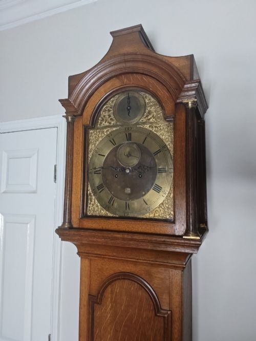 fig 2. An Early Georgian floor-standing oak longcase clock featuring a carved arch hood, brass dial with strike and silent selector, and a slim trunk door.