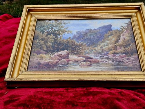 fig 1. A nineteenth-century watercolour landscape painting depicting a rocky river stream surrounded by foliage, mounted in a moulded gold gilt frame.