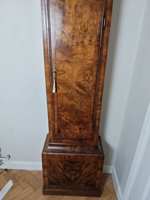 fig 1. An early Georgian longcase clock featuring a burr walnut veneered case, an arched hood, and a brass dial with Roman numerals.