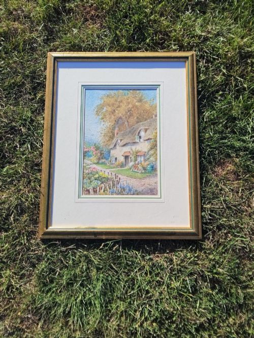 fig 2. A framed vertical watercolour painting depicting a traditional thatched cottage with a garden filled with colourful flowers under a blue sky.