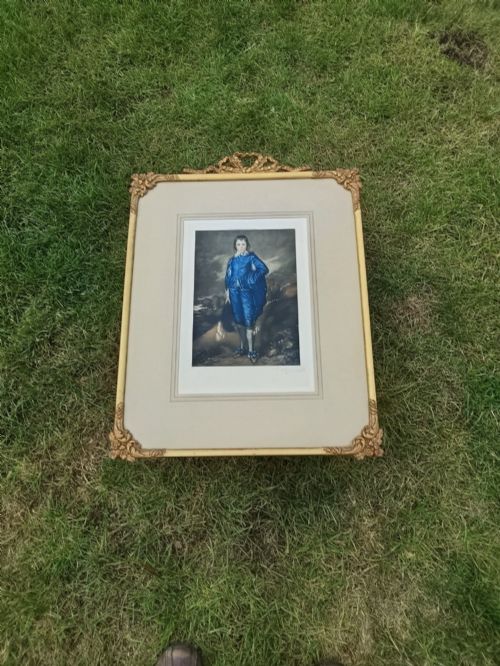 fig 1. A framed colour portrait print of Thomas Gainsboroughs The Blue Boy, set within a wide beige mount and a gold giltwood frame topped with a bow cresting.