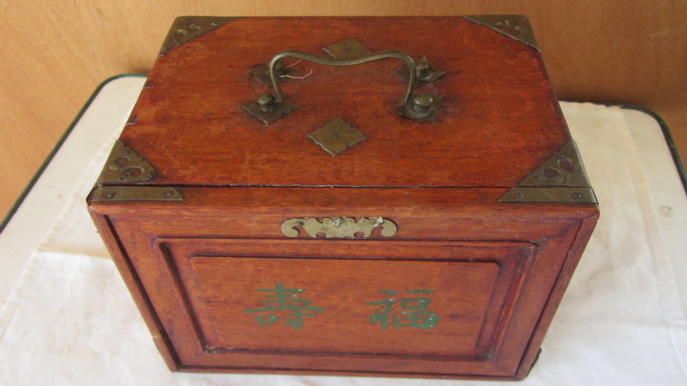 An early 20th-century wooden mahjong chest featuring brass corner mounts, a carrying handle, and green painted Chinese characters on the sliding front panel.