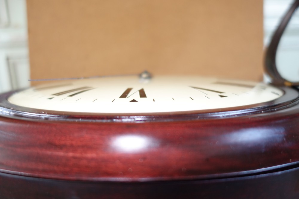 A circular antique mahogany wall clock with a convex glass face, brass bezel, and cream dial displaying black Roman numerals. View III