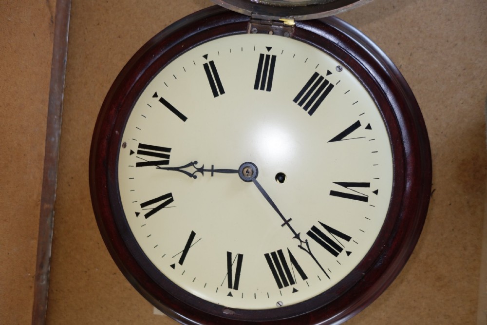 A circular antique mahogany wall clock with a convex glass face, brass bezel, and cream dial displaying black Roman numerals. View IX