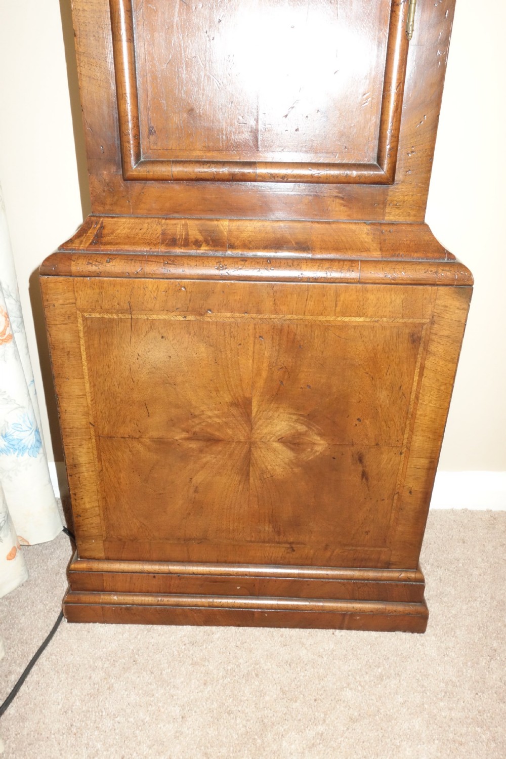 An early Georgian walnut longcase clock featuring a brass dial with Roman numerals, flanked by columns on the hood and a veneered wooden cabinet door. View III