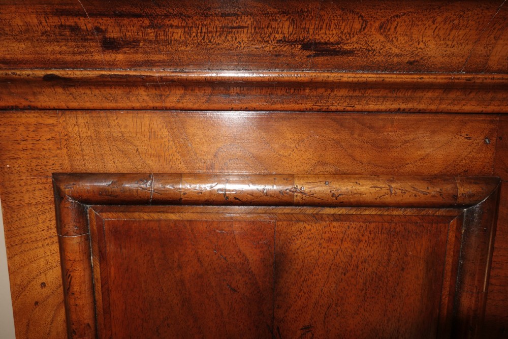 An early Georgian walnut longcase clock featuring a brass dial with Roman numerals, flanked by columns on the hood and a veneered wooden cabinet door. View IV