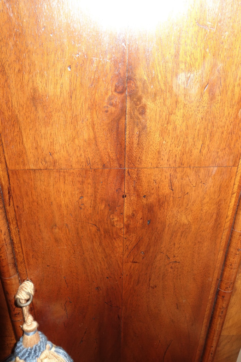 An early Georgian walnut longcase clock featuring a brass dial with Roman numerals, flanked by columns on the hood and a veneered wooden cabinet door. View V