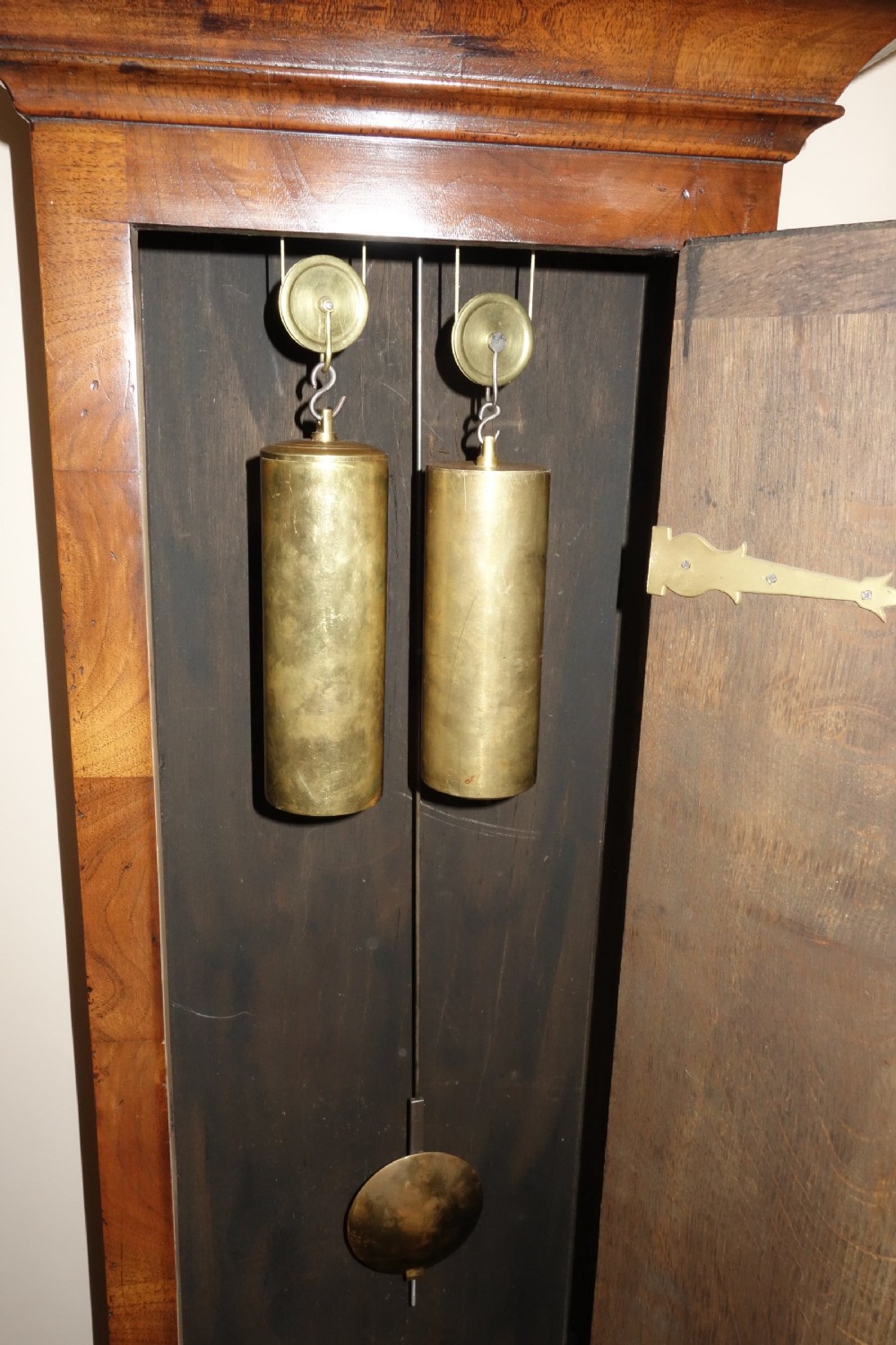 An early Georgian walnut longcase clock featuring a brass dial with Roman numerals, flanked by columns on the hood and a veneered wooden cabinet door. View VI