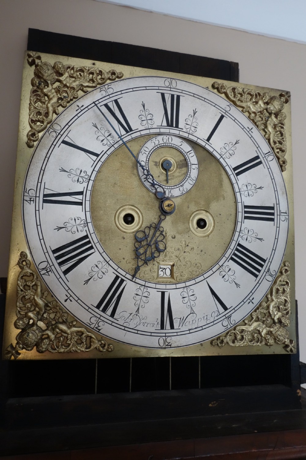 An early Georgian walnut longcase clock featuring a brass dial with Roman numerals, flanked by columns on the hood and a veneered wooden cabinet door. View VII