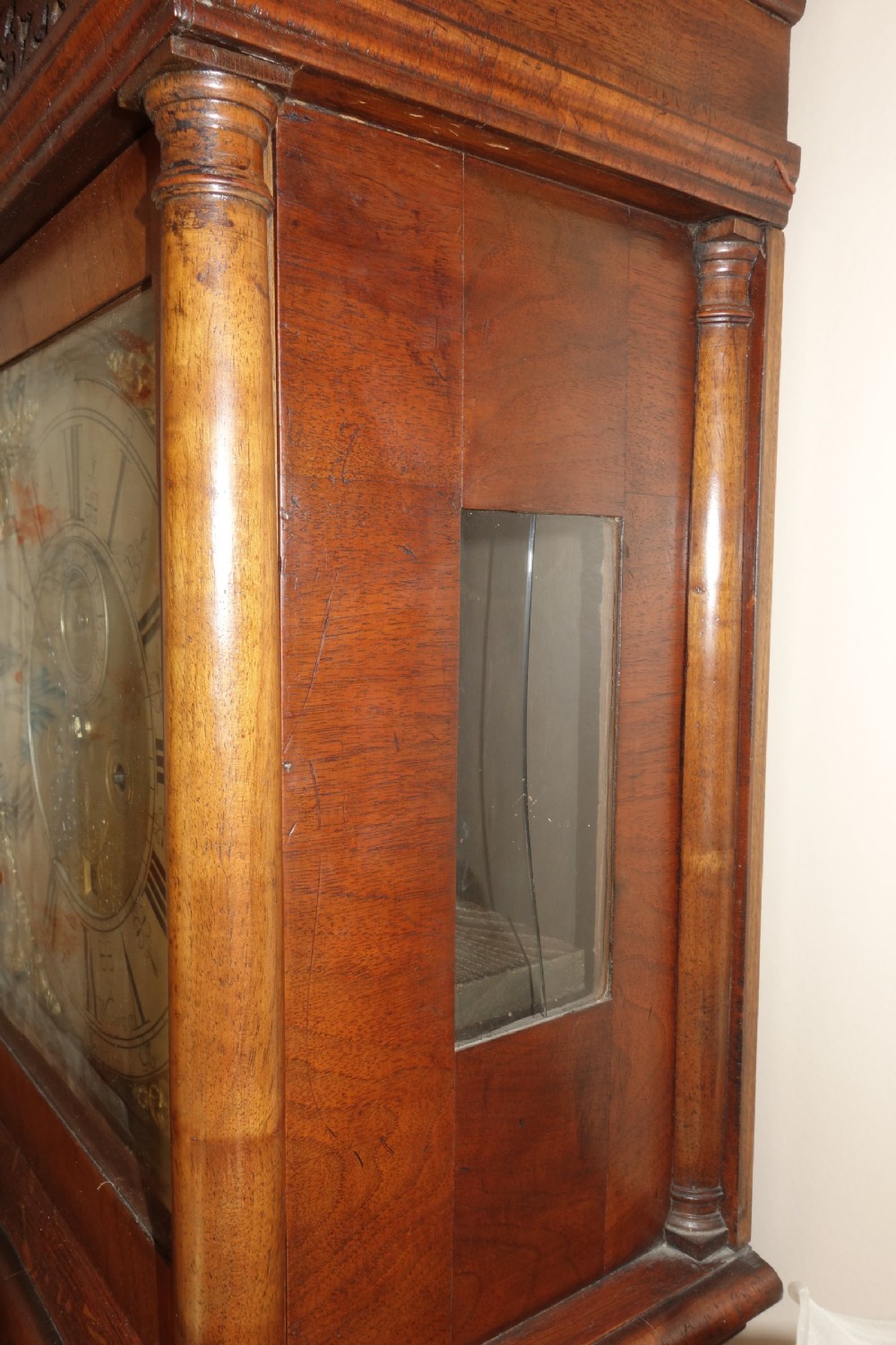 An early Georgian walnut longcase clock featuring a brass dial with Roman numerals, flanked by columns on the hood and a veneered wooden cabinet door. View XI