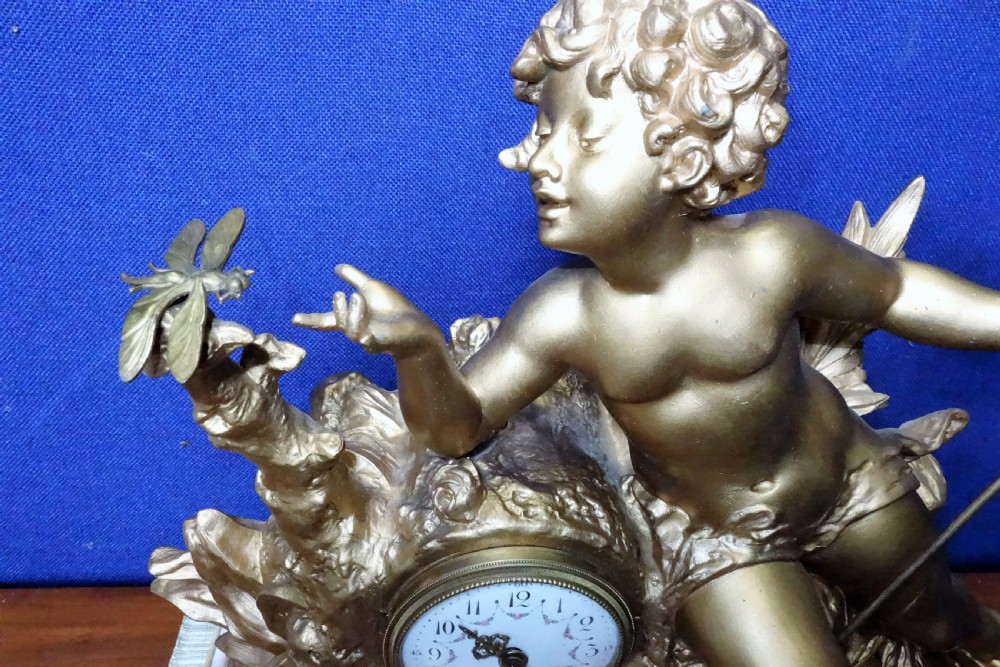 A nineteenth-century French gilt metal mantel clock featuring a sculpted cherub reaching for a dragonfly, mounted atop a variegated marble base. View II