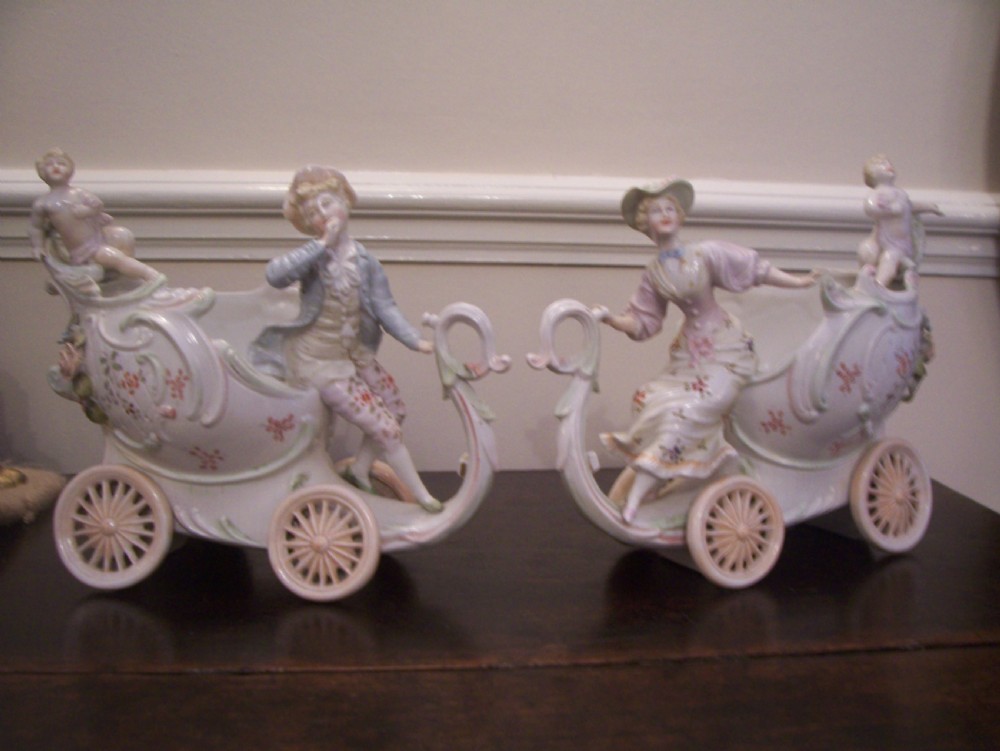 A pair of 19th-century pastel porcelain chariot vases featuring sculpted male and female figures with cherubs and scroll details.