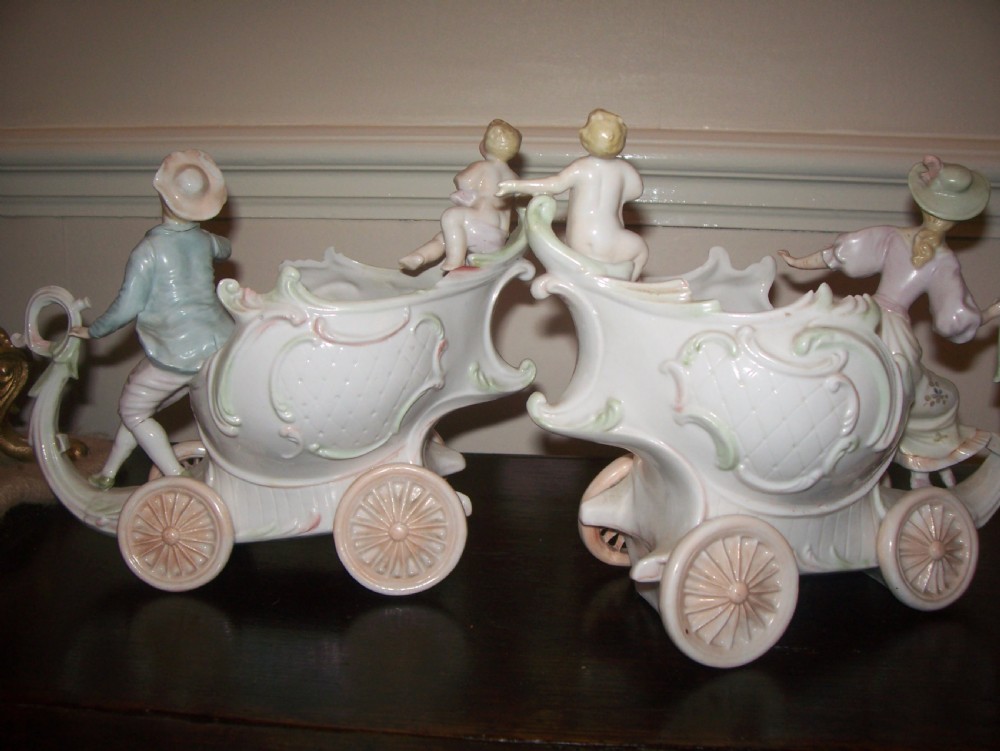 A pair of 19th-century pastel porcelain chariot vases featuring sculpted male and female figures with cherubs and scroll details. View IX