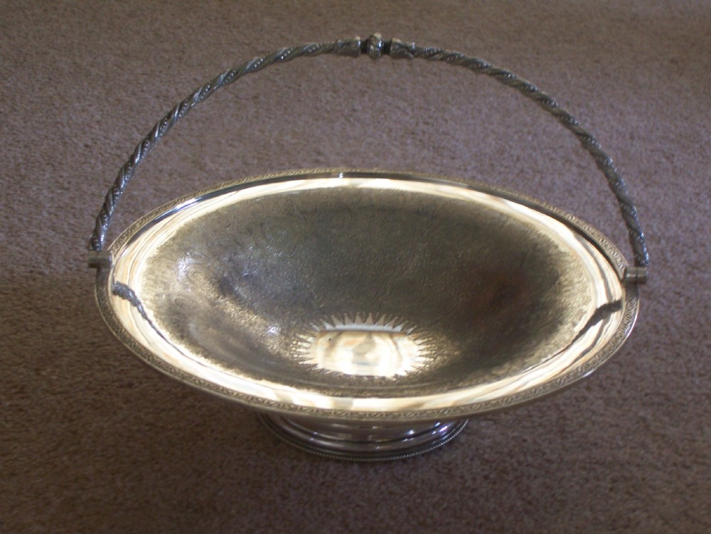 A Victorian silver-plated oval cake basket featuring a twisted overhead swing handle and a raised pedestal base. View II