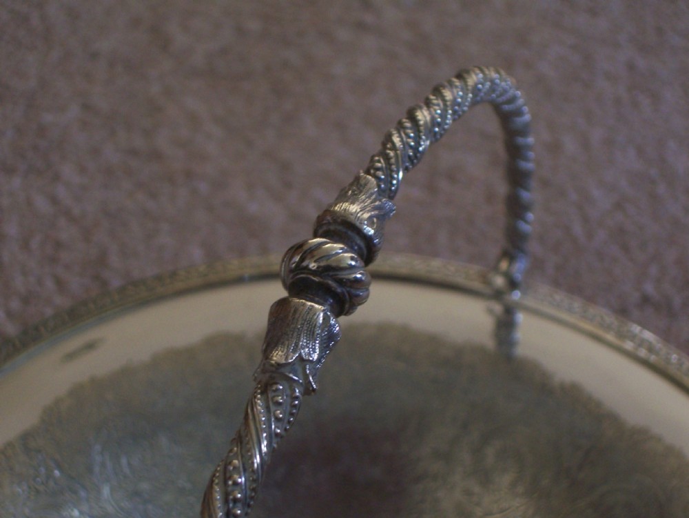 A Victorian silver-plated oval cake basket featuring a twisted overhead swing handle and a raised pedestal base. View IV