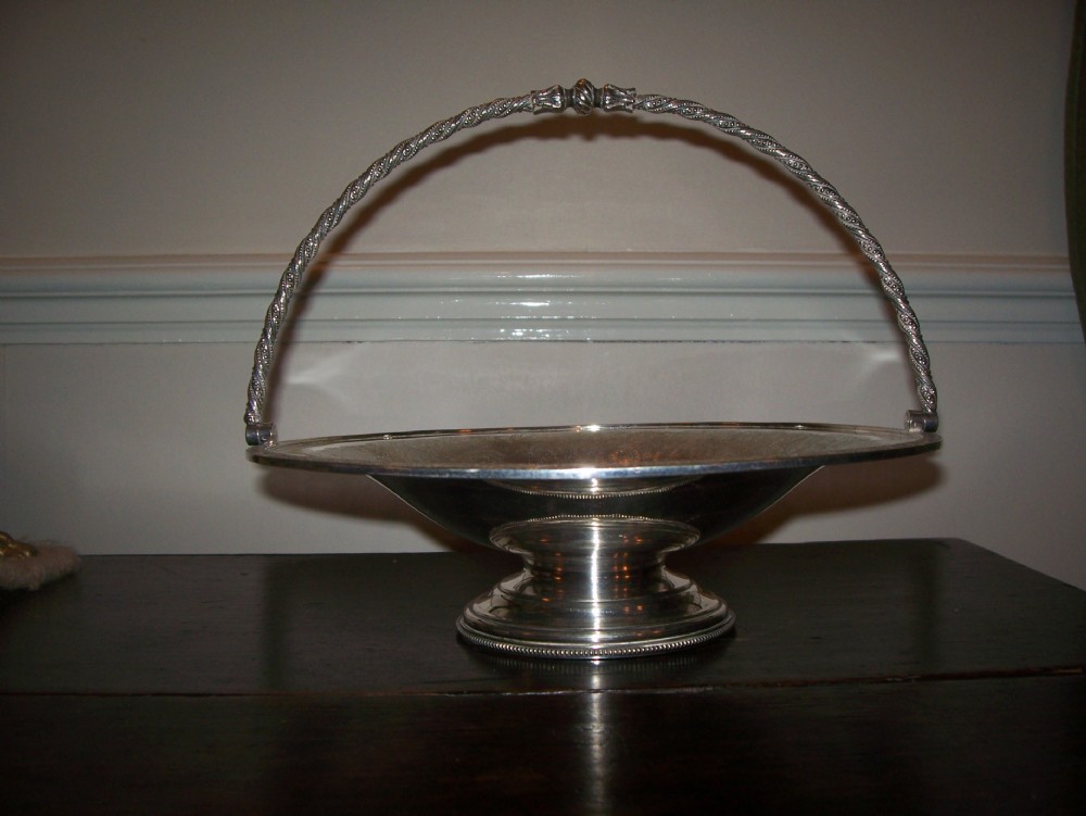 A Victorian silver-plated oval cake basket featuring a twisted overhead swing handle and a raised pedestal base.