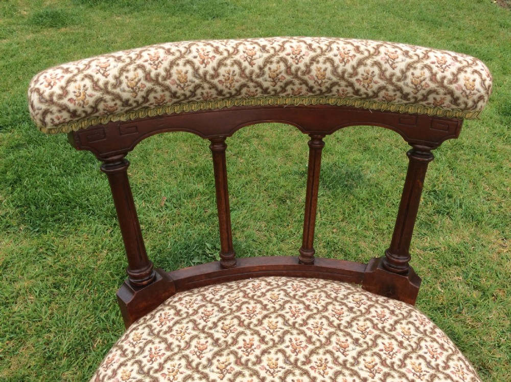 A Victorian low-seated nursing chair featuring a dark mahogany spindle back, padded top rail, pattern-upholstered seat with fringe trim, and turned front legs with castors. View II