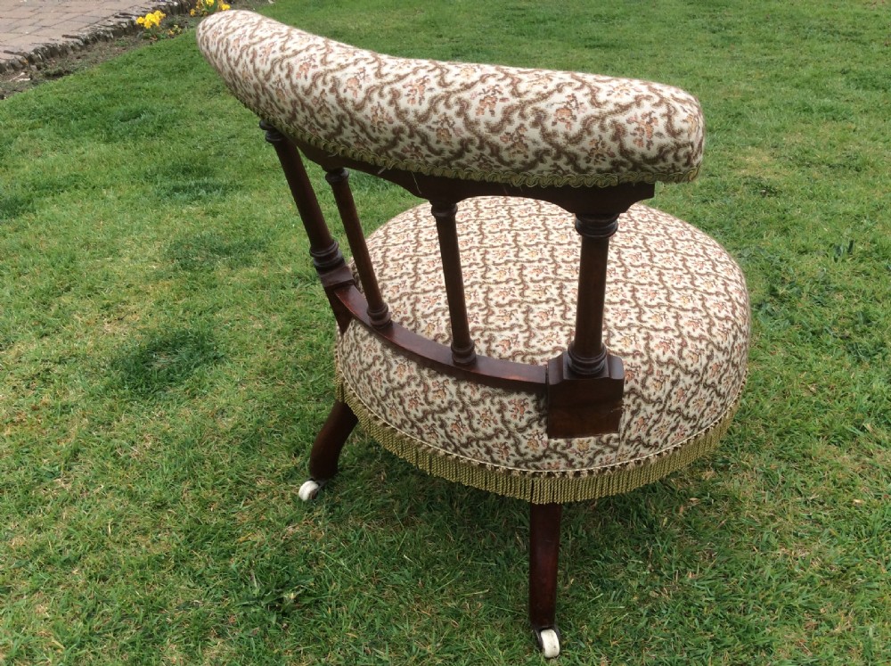 A Victorian low-seated nursing chair featuring a dark mahogany spindle back, padded top rail, pattern-upholstered seat with fringe trim, and turned front legs with castors. View III