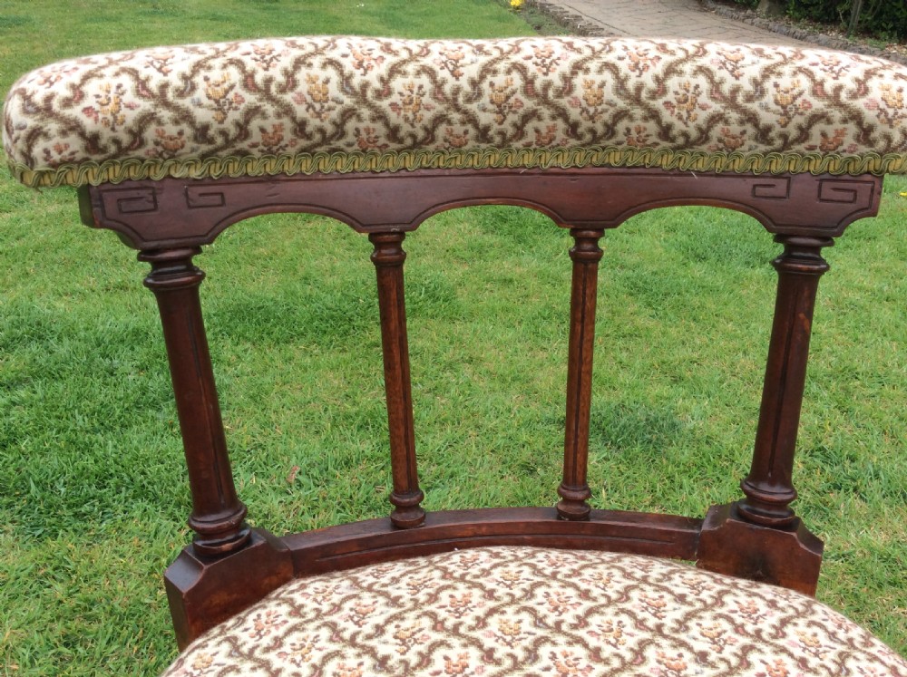 A Victorian low-seated nursing chair featuring a dark mahogany spindle back, padded top rail, pattern-upholstered seat with fringe trim, and turned front legs with castors. View V