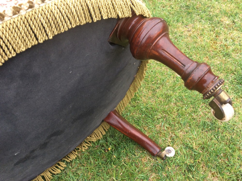 A Victorian low-seated nursing chair featuring a dark mahogany spindle back, padded top rail, pattern-upholstered seat with fringe trim, and turned front legs with castors. View VI