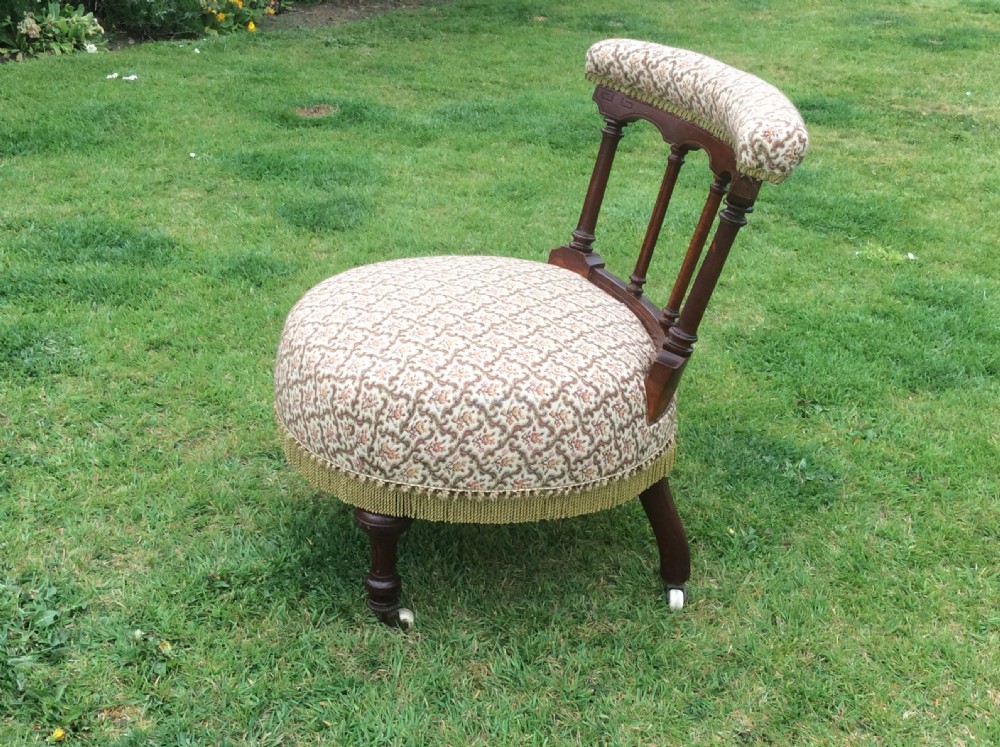 A Victorian low-seated nursing chair featuring a dark mahogany spindle back, padded top rail, pattern-upholstered seat with fringe trim, and turned front legs with castors. View VIII