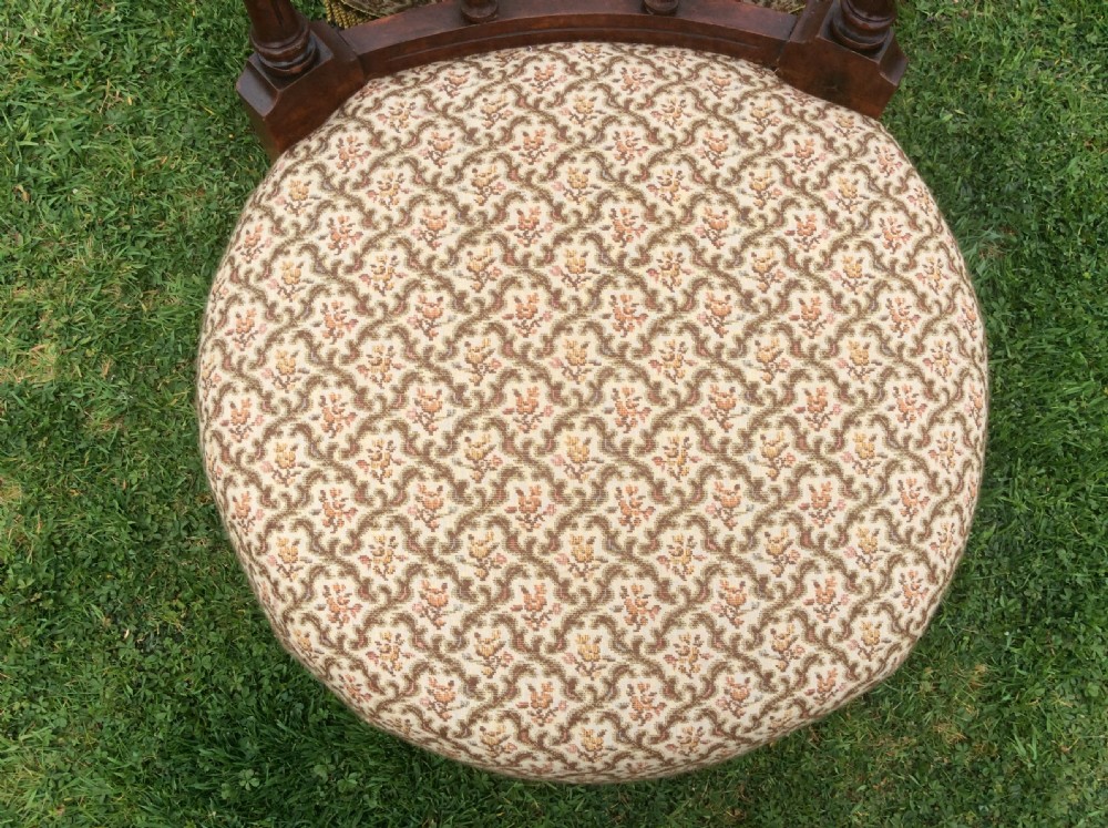 A Victorian low-seated nursing chair featuring a dark mahogany spindle back, padded top rail, pattern-upholstered seat with fringe trim, and turned front legs with castors. View XII