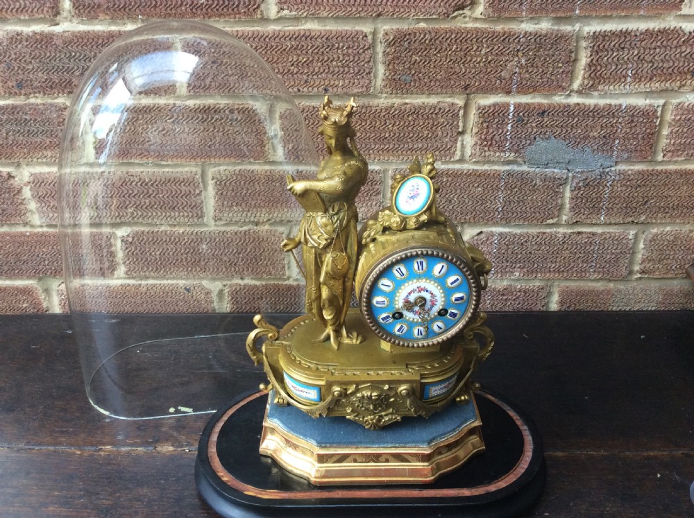 A mid nineteenth-century French gilt ormolu mantel clock featuring a classical figure, blue Sevres-style porcelain dial, and panels, set under a clear glass dome on a wooden base. View II