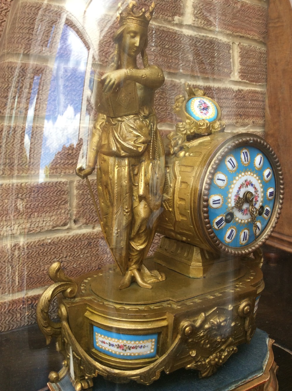 A mid nineteenth-century French gilt ormolu mantel clock featuring a classical figure, blue Sevres-style porcelain dial, and panels, set under a clear glass dome on a wooden base. View III