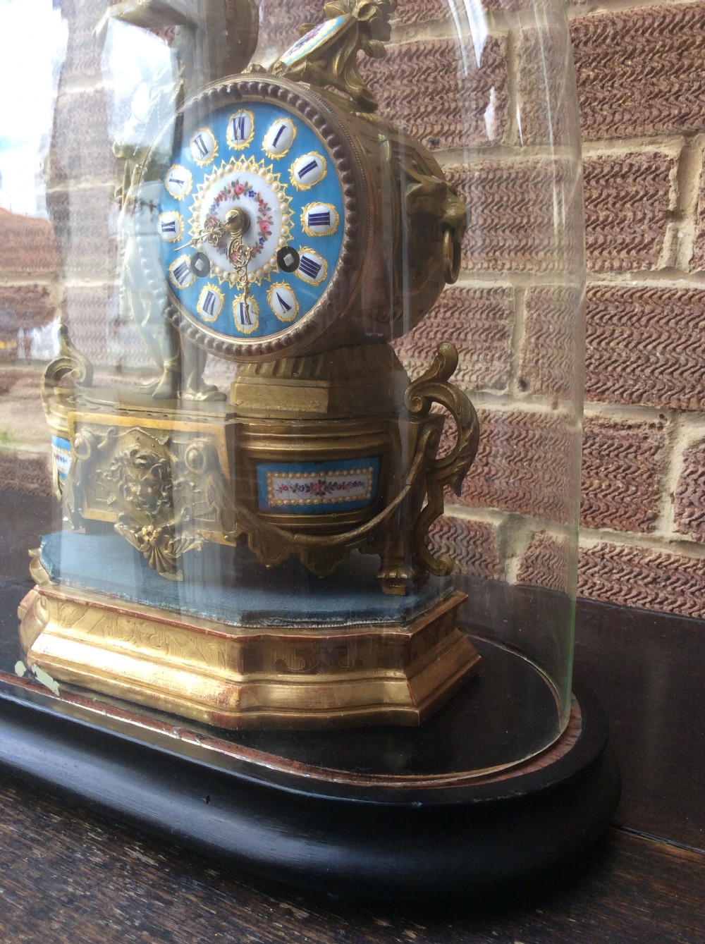 A mid nineteenth-century French gilt ormolu mantel clock featuring a classical figure, blue Sevres-style porcelain dial, and panels, set under a clear glass dome on a wooden base. View IV