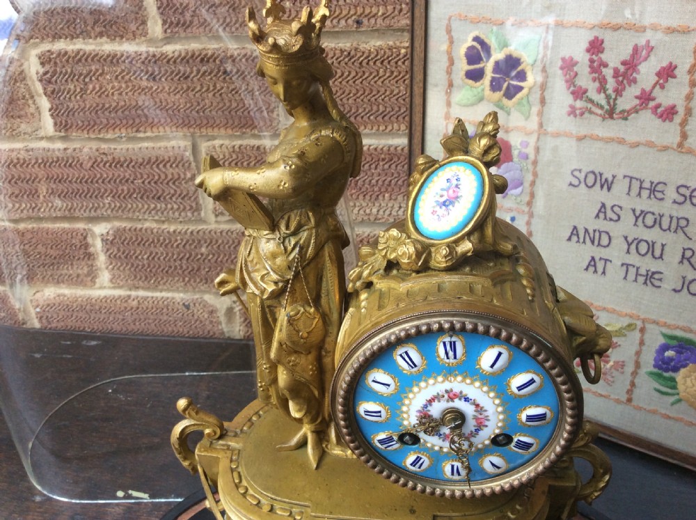 A mid nineteenth-century French gilt ormolu mantel clock featuring a classical figure, blue Sevres-style porcelain dial, and panels, set under a clear glass dome on a wooden base. View X