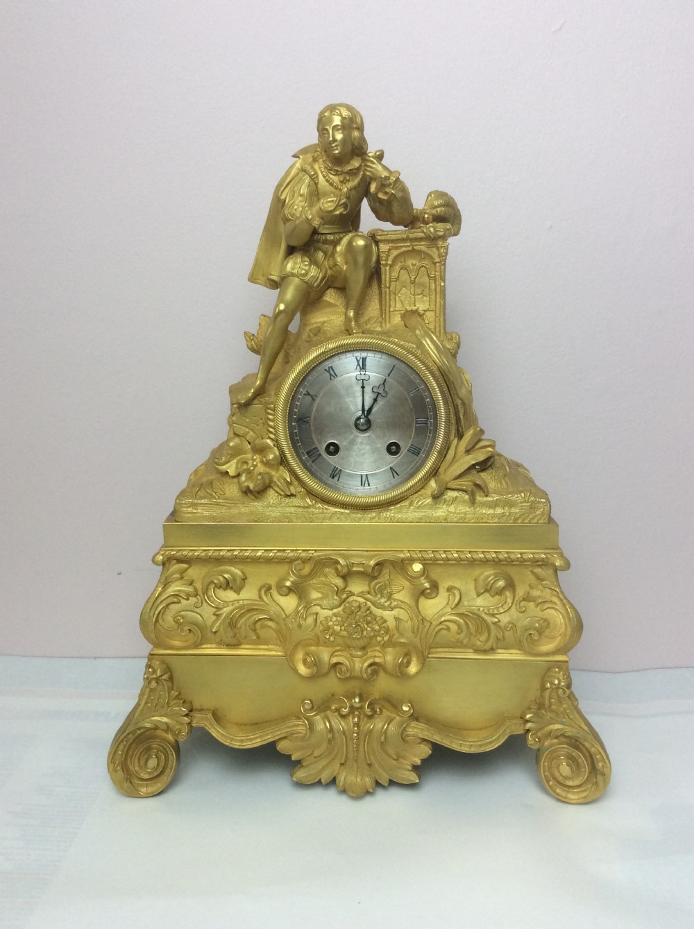 A gilt bronze French Empire mantel clock featuring a sculpted explorer figure sitting above a silvered dial on an ornate scrollwork base.