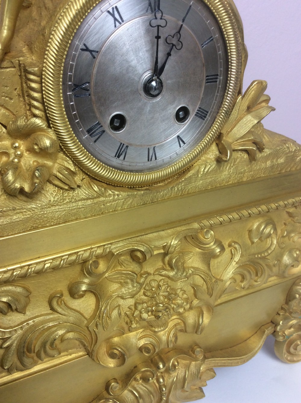 A gilt bronze French Empire mantel clock featuring a sculpted explorer figure sitting above a silvered dial on an ornate scrollwork base. View V