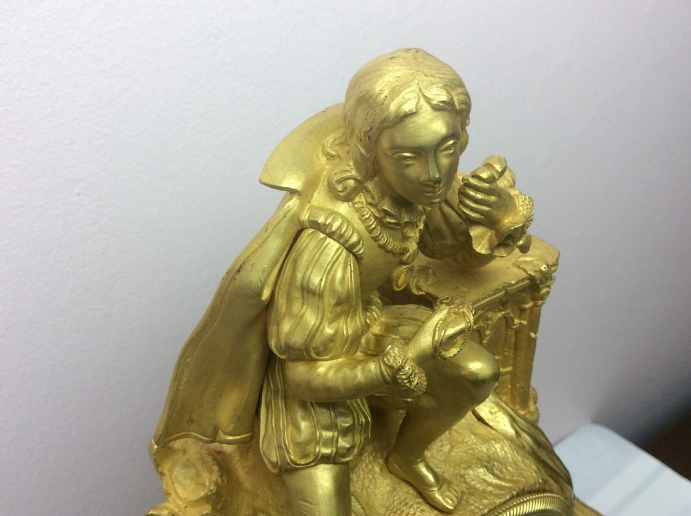 A gilt bronze French Empire mantel clock featuring a sculpted explorer figure sitting above a silvered dial on an ornate scrollwork base. View VI